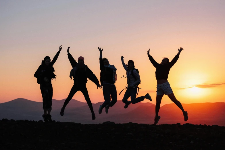 a group of people jumping in the air in the sunset