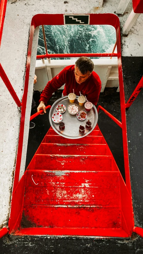 man eating food on red stairs next to the water