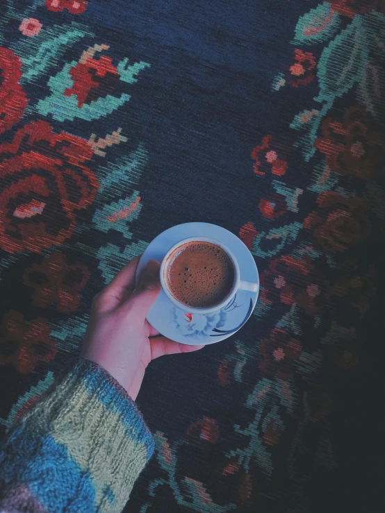 a person holding a cup of coffee on a floral rug