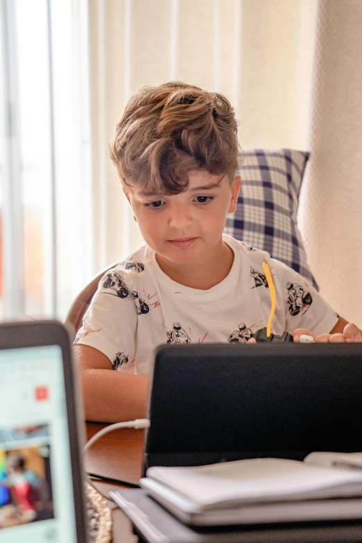 a small boy is looking at a laptop with an apple pencil