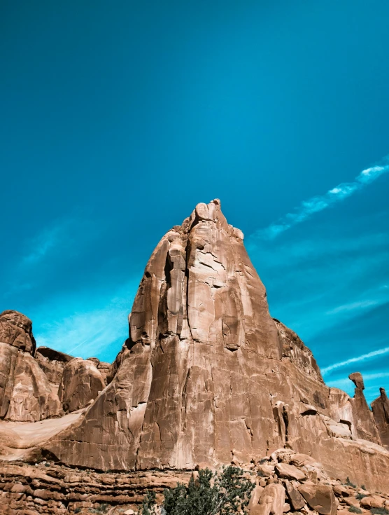 large rock formation in a desert area under a cloudy blue sky