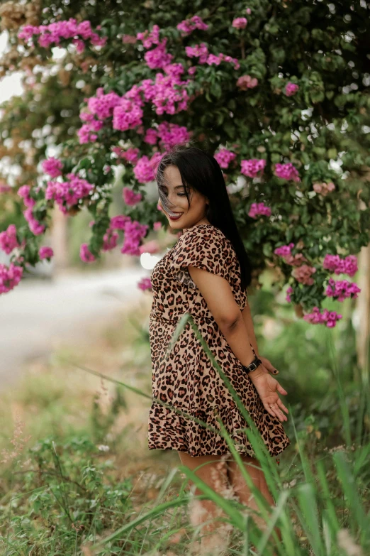 a young woman in a leopard print dress leaning on a bush