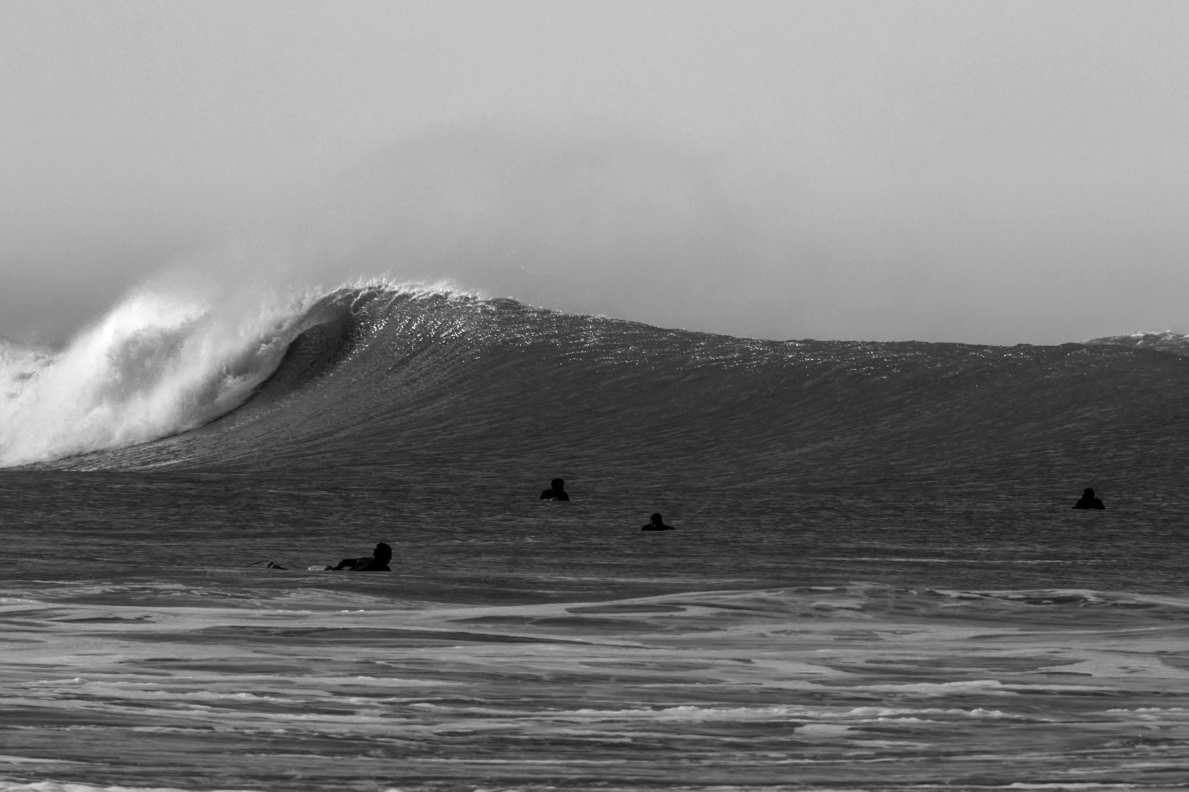 the ocean waves are white as the three surfers ride the wave