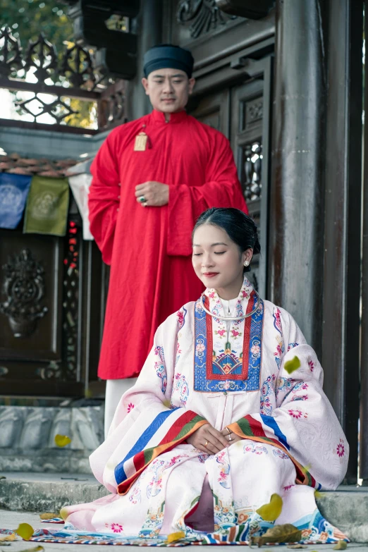 a woman in a red outfit sitting on the ground next to another man wearing a red suit