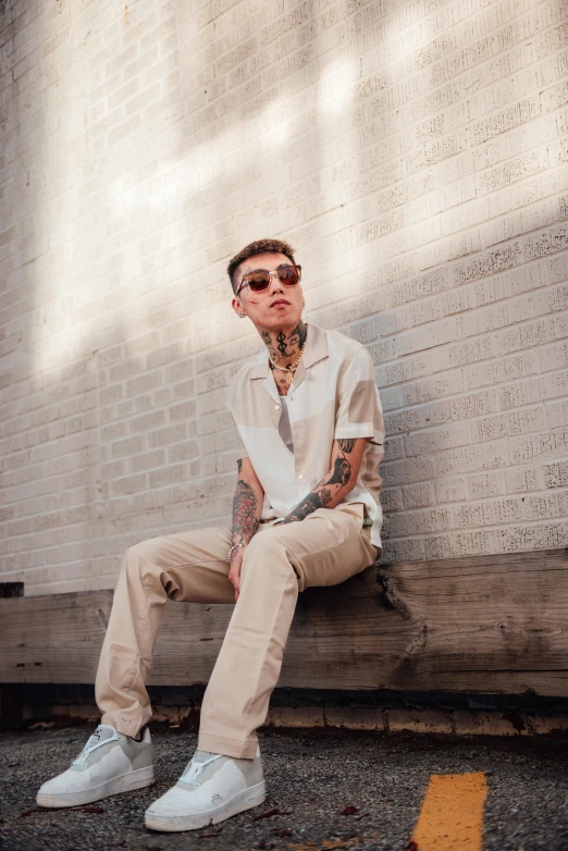 a young man wearing glasses is sitting on a curb