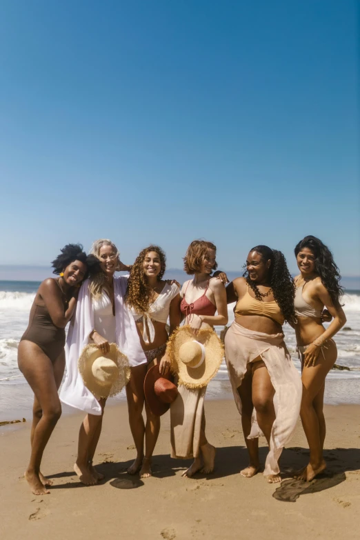 six women posing on the beach wearing hats