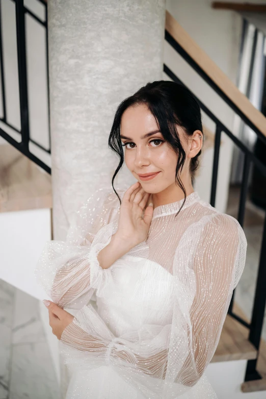 a woman is dressed in a long sleeved wedding gown and posing on the staircase