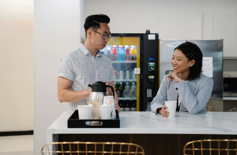 a man and woman preparing their drinks in the kitchen