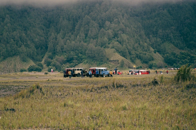 the group of trucks are parked in the field by a mountain