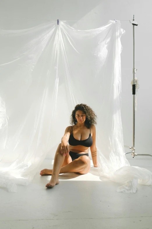 a young lady in a black bikini sitting on a bed covered with sheer fabric