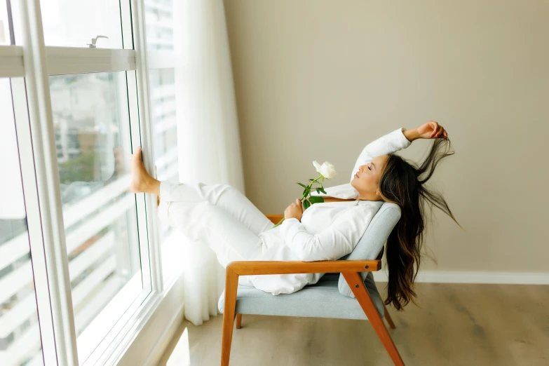 a beautiful young lady sitting in a chair holding a flower