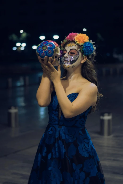 a  in a blue dress wearing a skull face painting holding up two balls