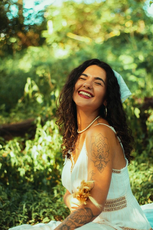 smiling woman sitting in the woods with her arm around her chest