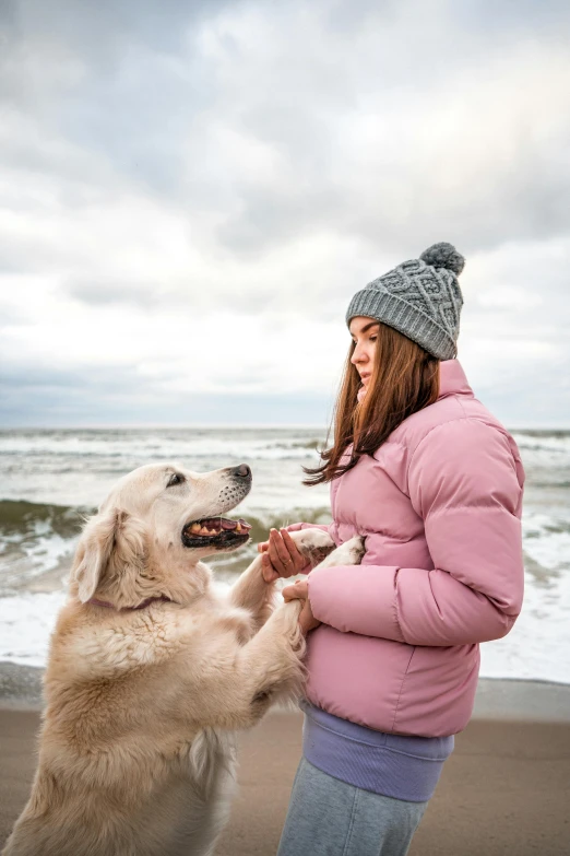 a girl plays with her dog in front of the ocean