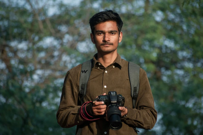 a man standing in front of trees with a camera in hand