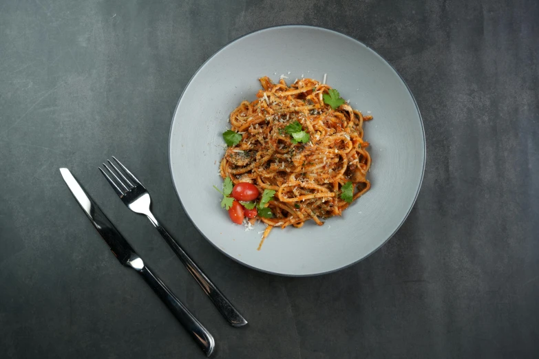 a bowl of pasta with tomatoes and a fork on a table