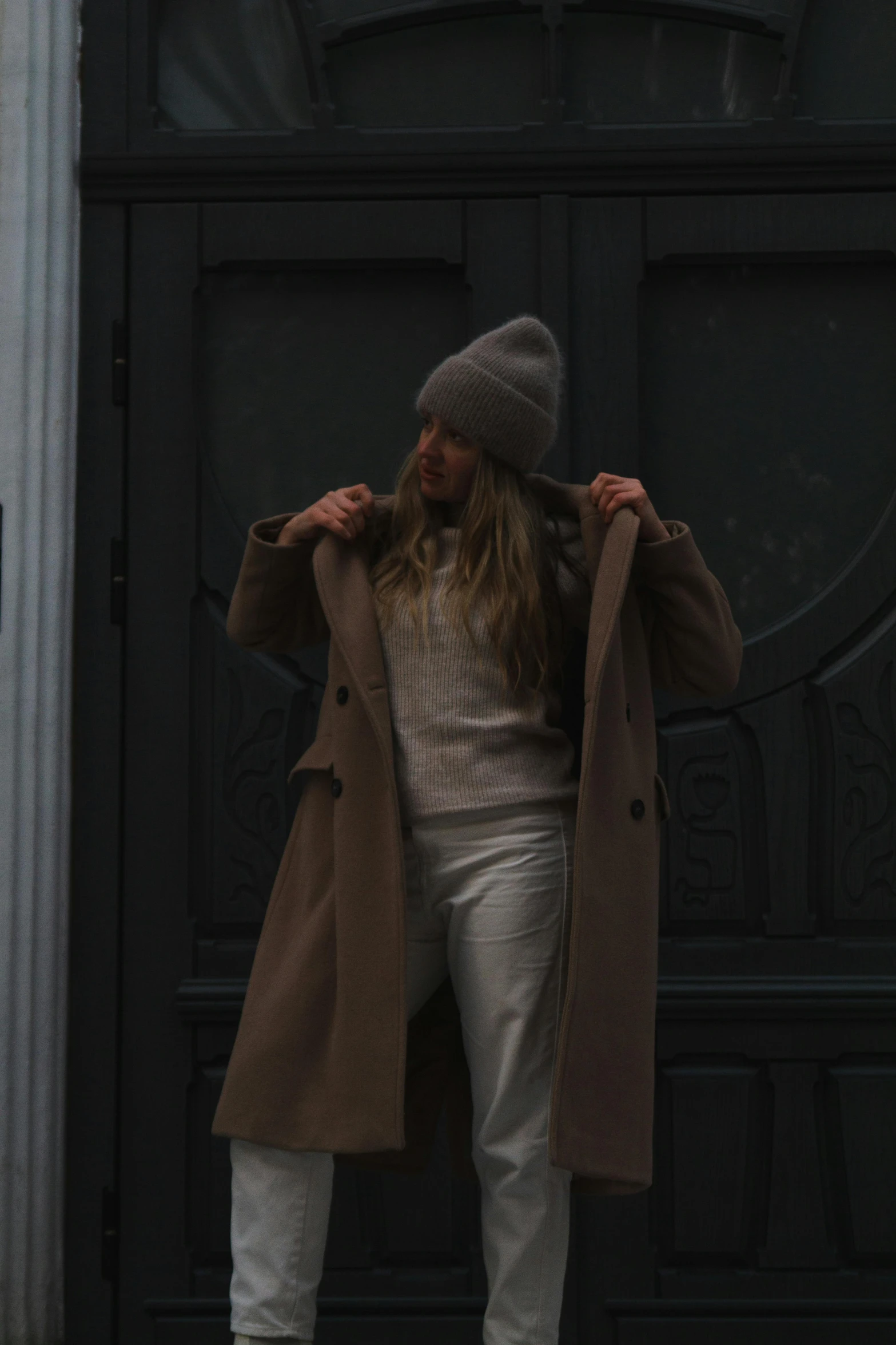 a woman wearing a hat, sweater and jacket standing on the street