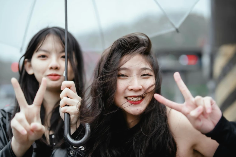 two woman holding up peace signs under an umbrella