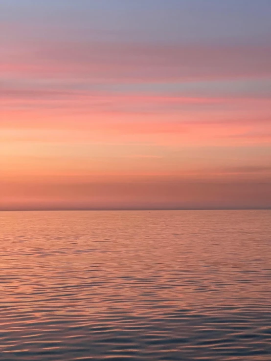 a large body of water with pink and purple clouds