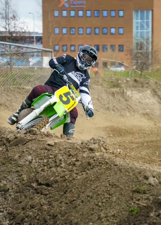 man on green dirt bike on mud track near building