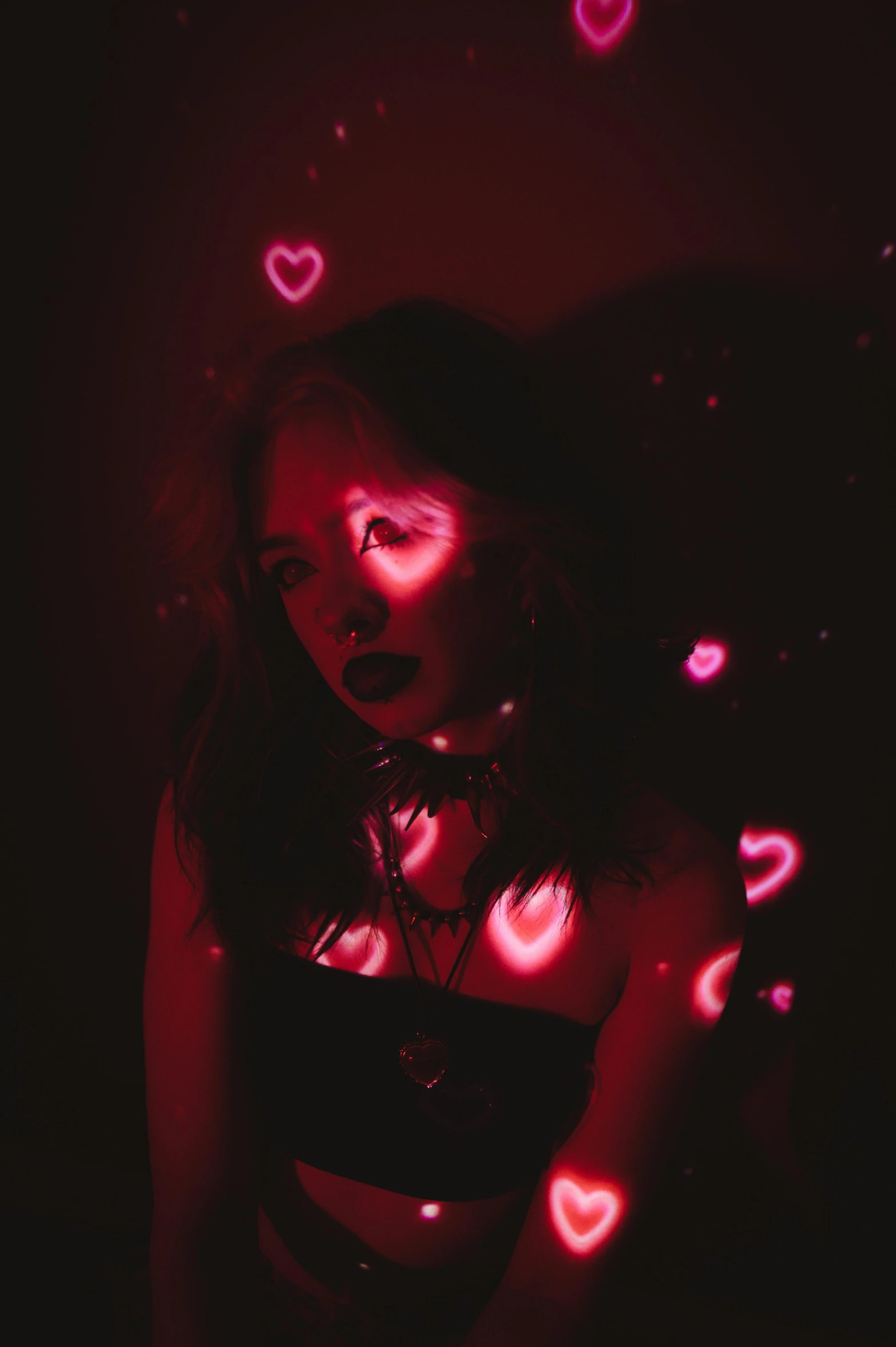 a woman in a revealing  posing in a dark room with lots of pink hearts floating all over her