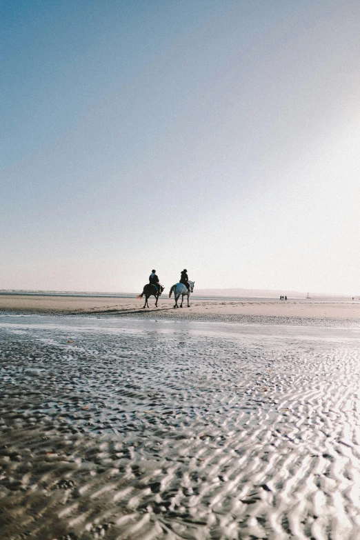 two people riding horses through shallow water on a beach