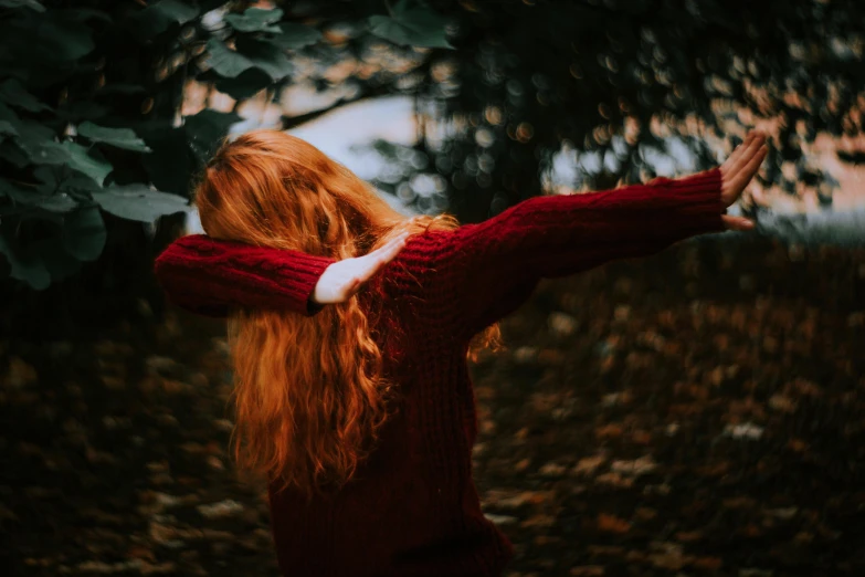 red haired girl walking on leaf covered ground with hand out