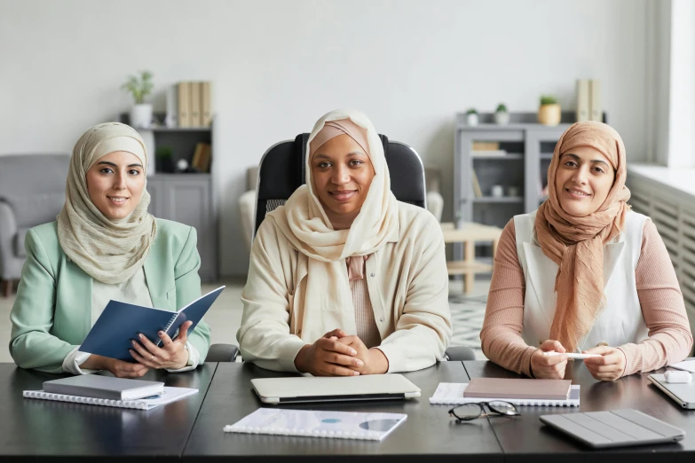 three women in hijabs sit at a table and study