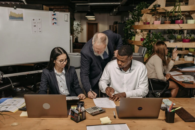 three people are looking at papers on their laptops