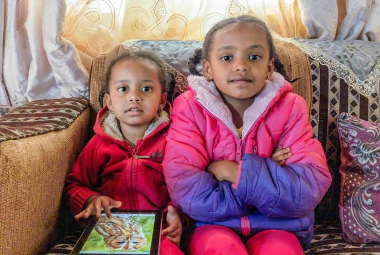 two s sitting on a couch, both wearing brightly colored coats