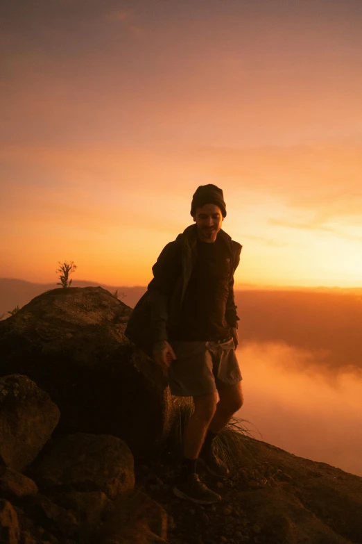 a man standing on a hill with sunset behind him