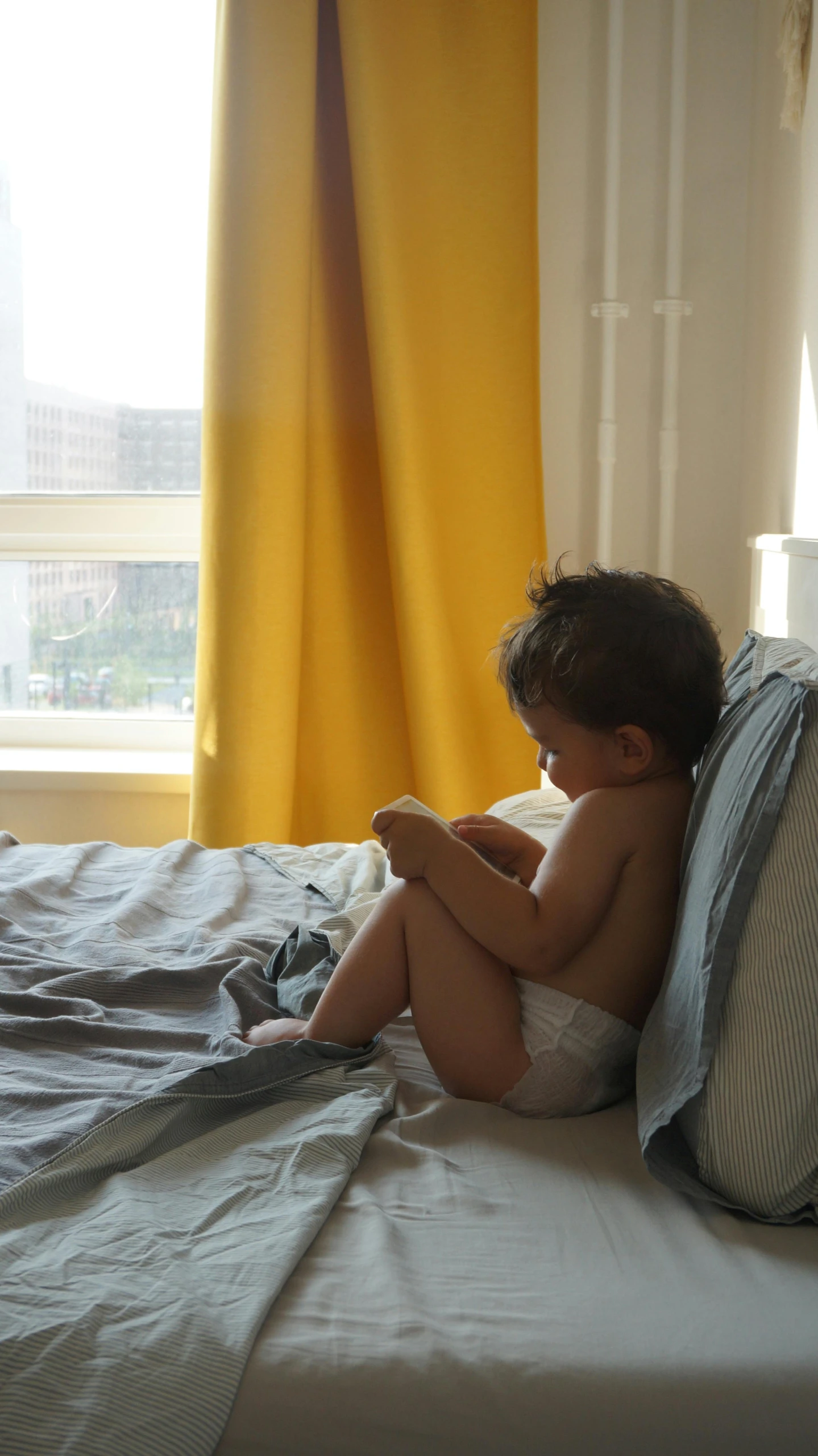 a toddler sits on a bed reading a book