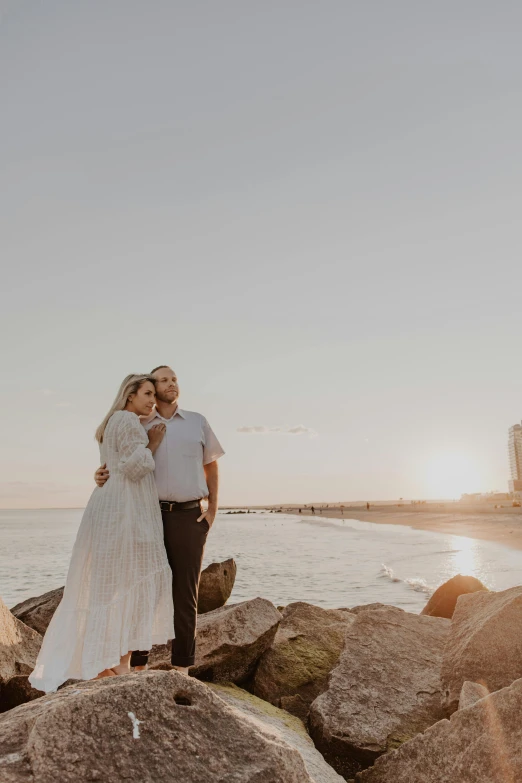 a man and woman are standing on the rocks together by the ocean