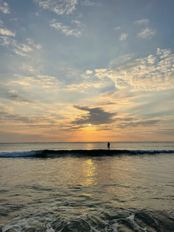 two people stand on the surfboard in front of the sun