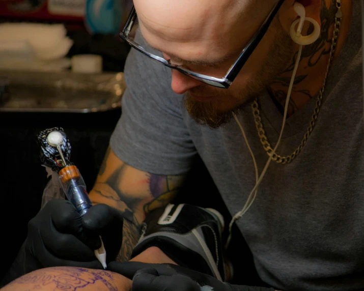 a tattooed man with glasses and a gray shirt holding onto a lighter