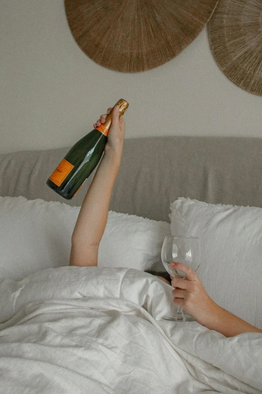 a woman laying in bed with her legs up on a pillow while holding a bottle of wine