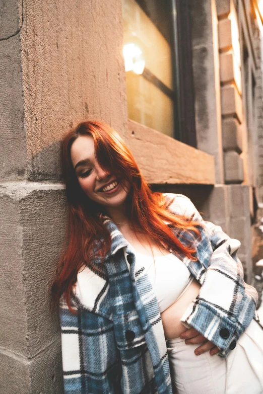 woman standing by wall in plaid jacket smiling at camera