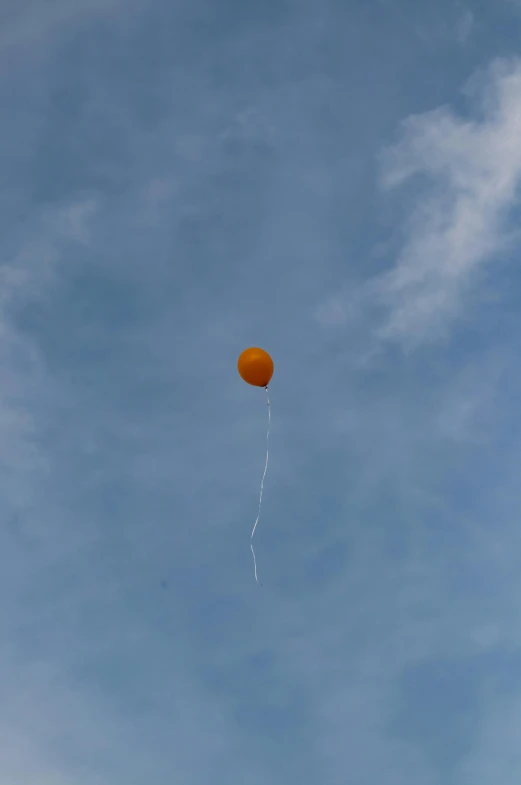 an orange balloon floating through a cloudy blue sky