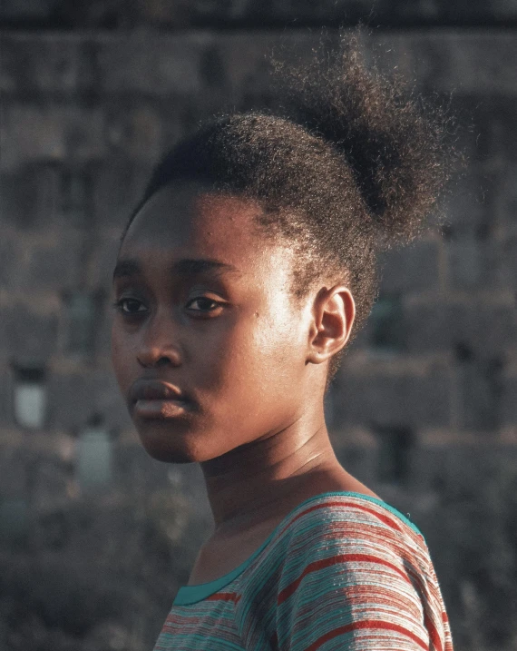 a black child in striped shirt standing next to a wall