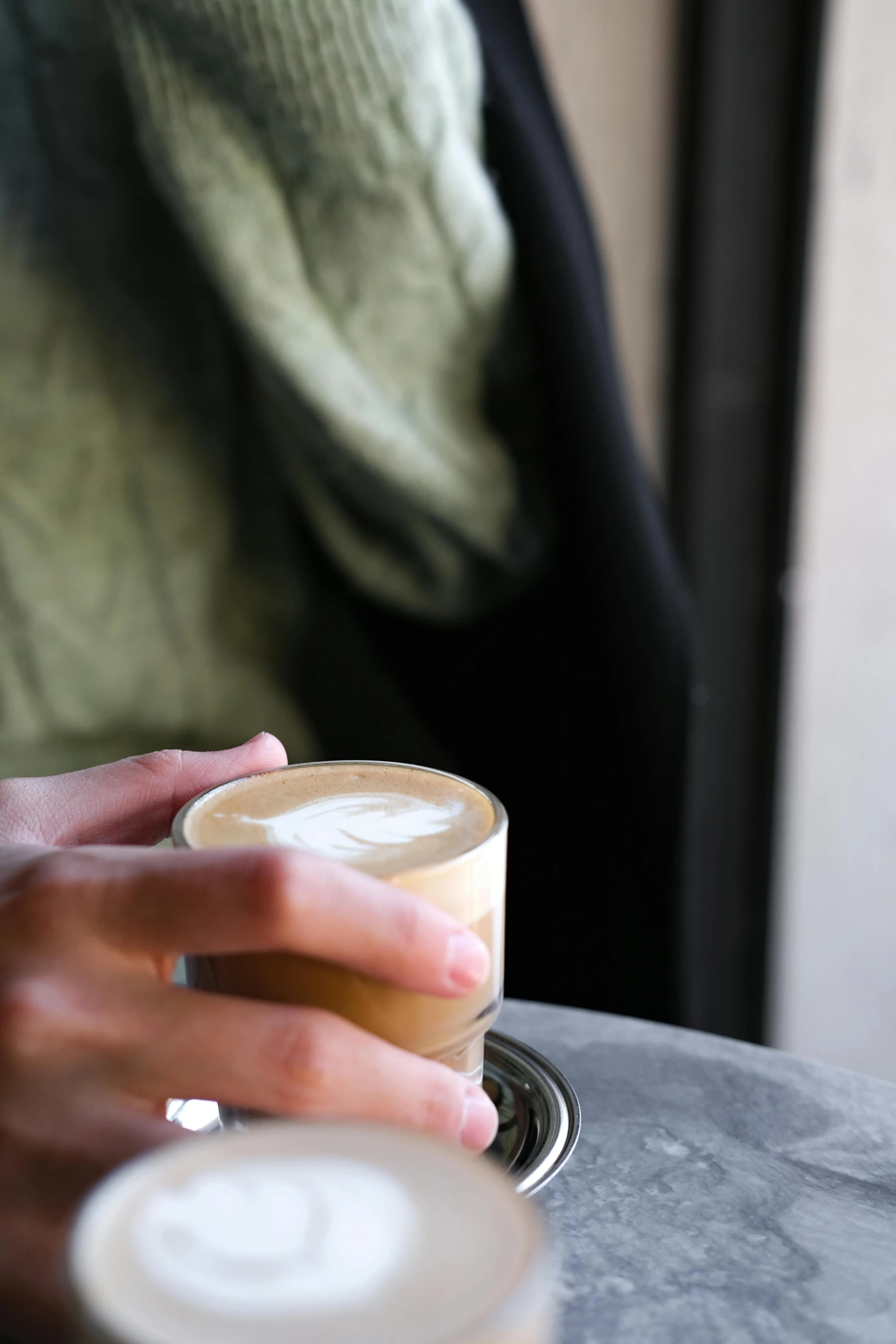 a person holding a cup of coffee next to a glass