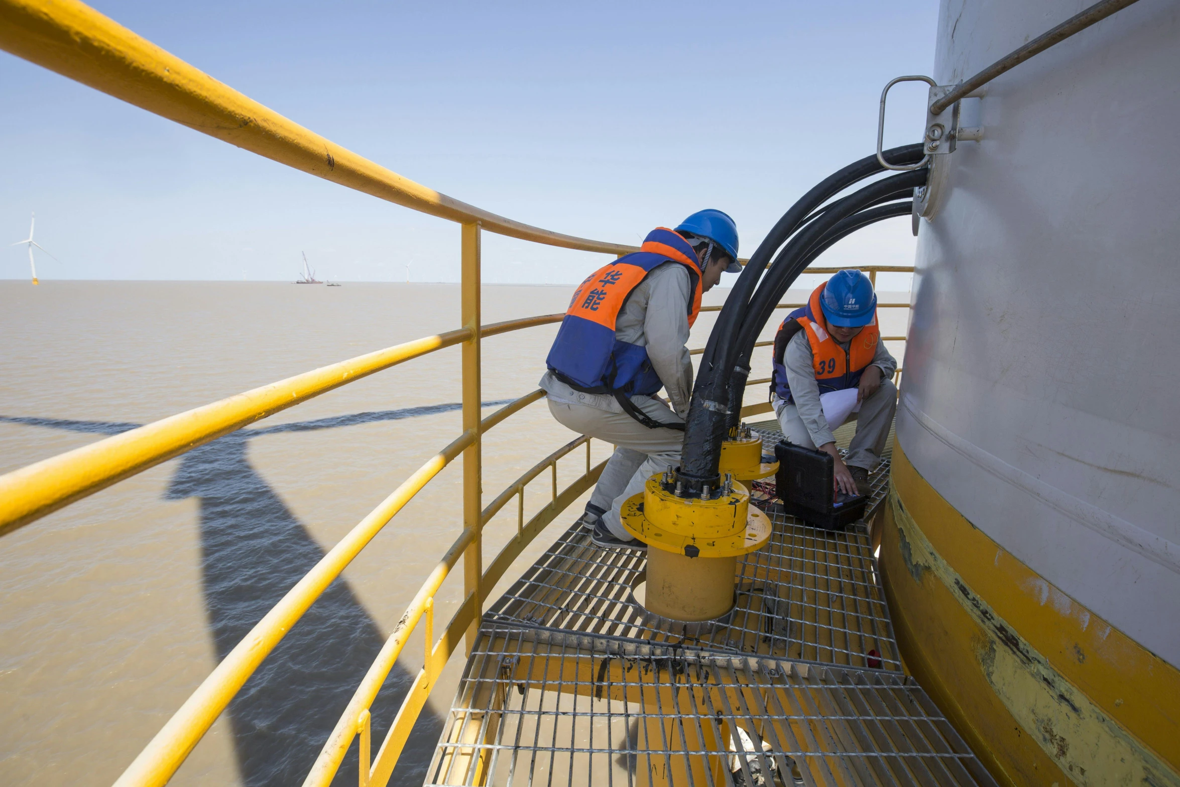 two workers attach soing in plastic containers on the side of a boat