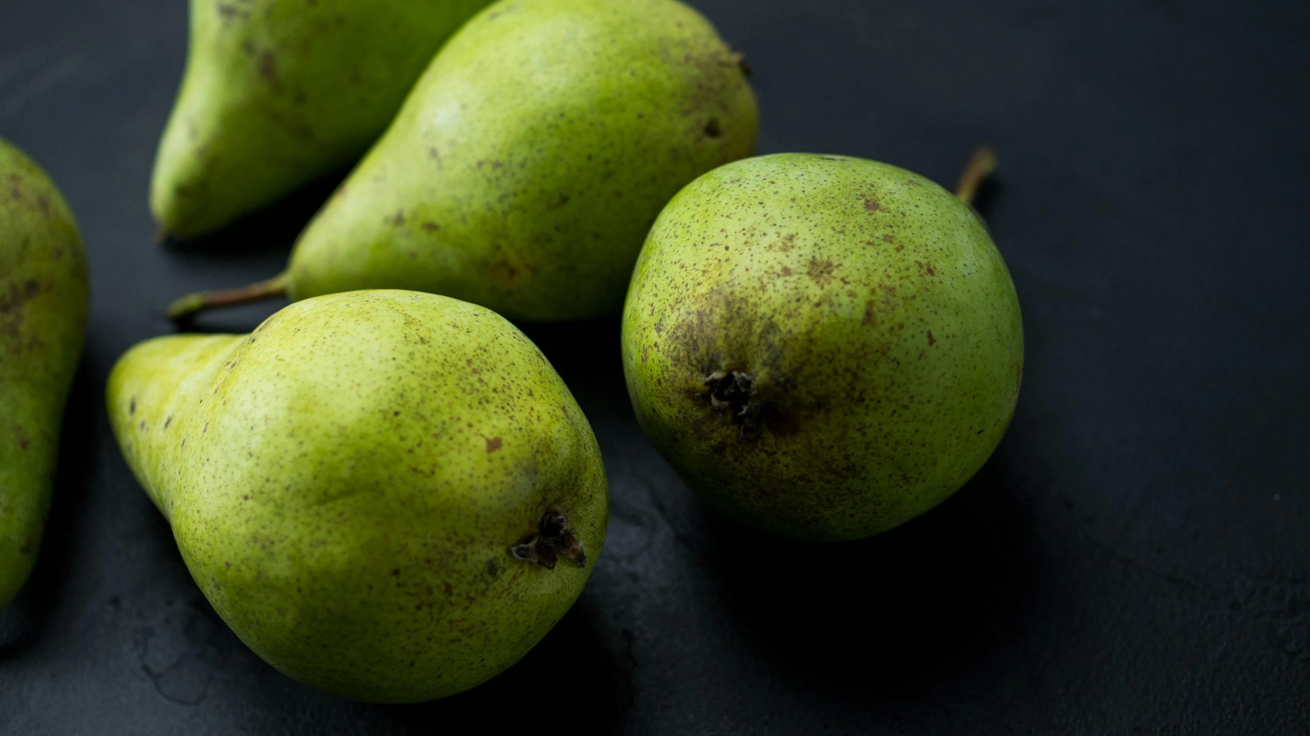 five green pears and some brown spots sitting on a table