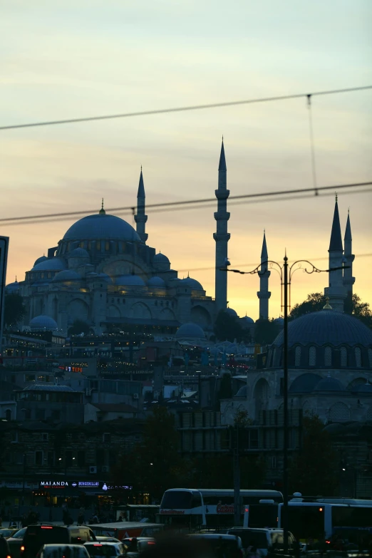 cars passing past large structures in city at dusk