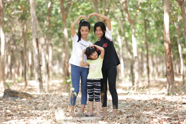 three women in the woods holding hands up to a heart