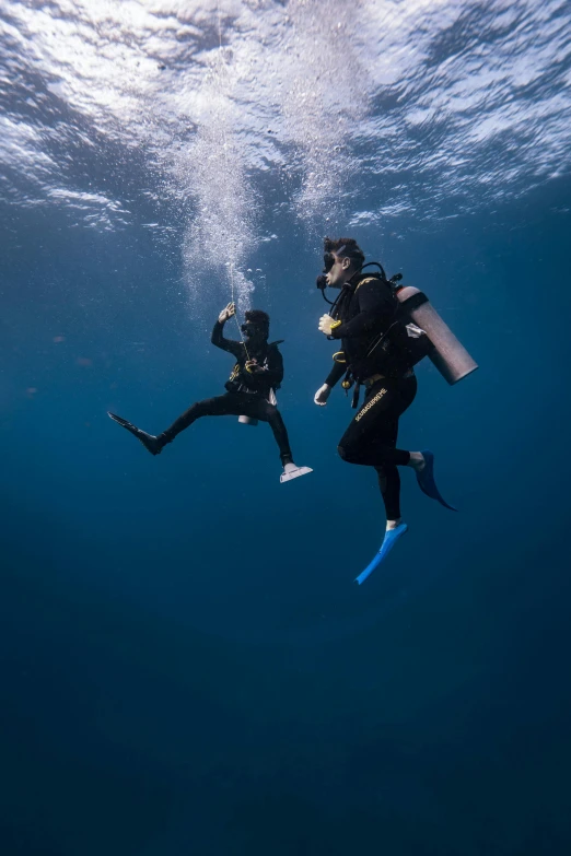 two scuba divers, one holding a camera, swim in the water