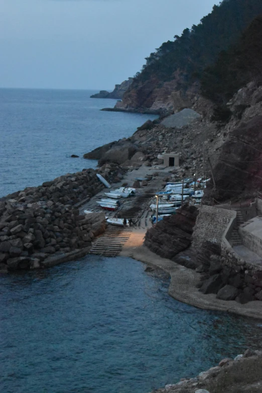 small beach on rocky coast by water with white and gray boats