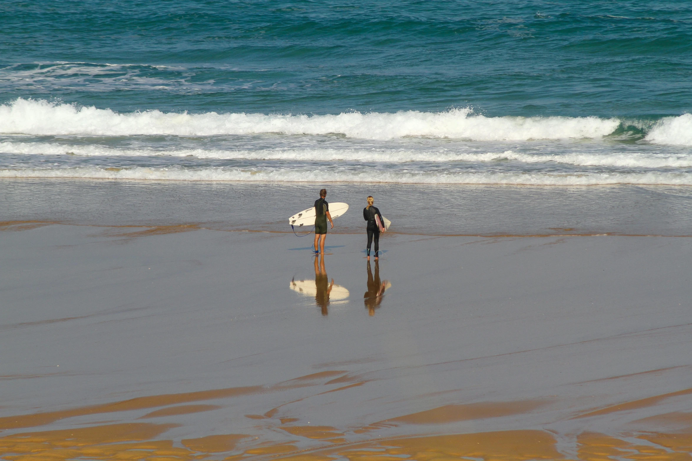 two people with surfboards walking along a beach