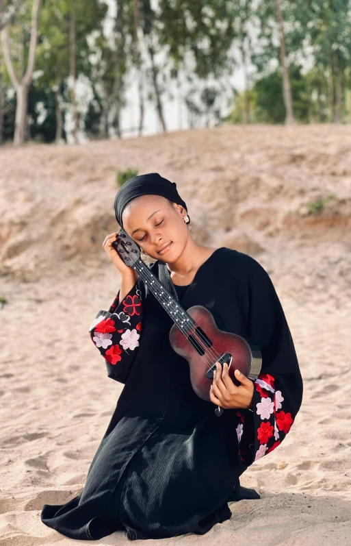 a woman in black dress with a guitar on the beach