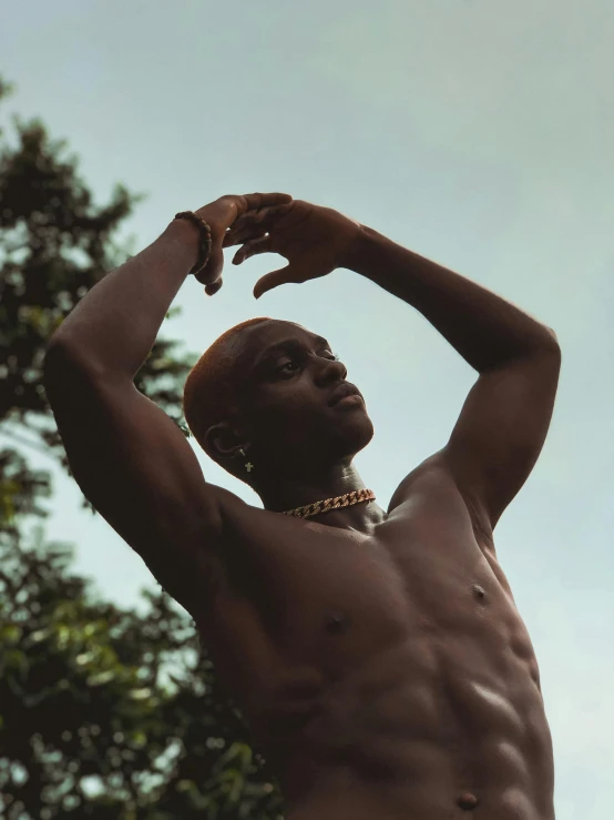 a shirtless man poses in front of trees