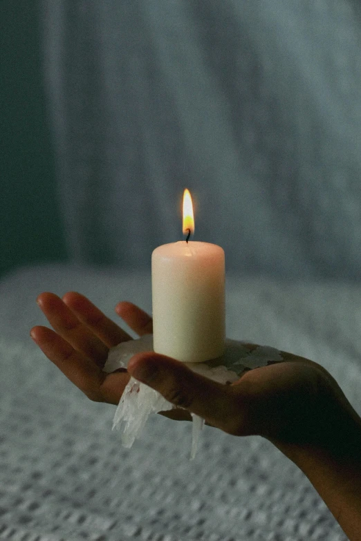 a hand holding a burning candle on a bed